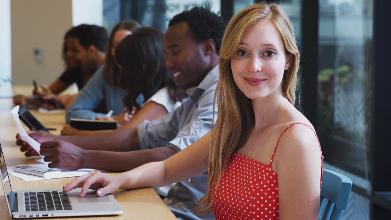 Portrait Of Businesswoman Working At Desk On Laptop In Shared Open Plan Office Workspace