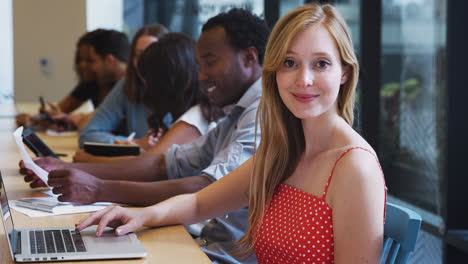 portrait of businesswoman working at desk on laptop in shared open plan office workspace