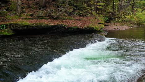 Stunning-low-drone-footage-of-stunning,-mossy-autumnal-woodland-stream-deep-in-the-mountains