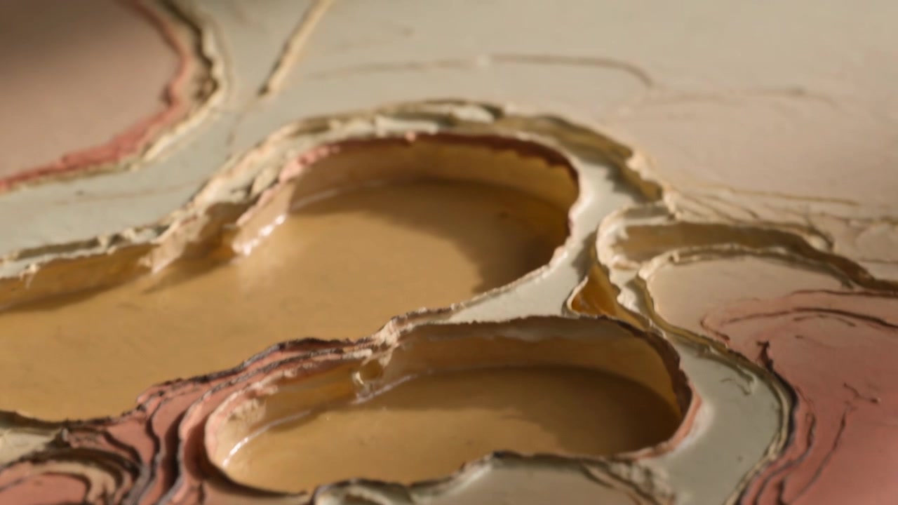 Et zoomende kamera avslører lagdelt pigment i glansfulle beige fordypninger på et bord, som viser tekstur og kontrast.
