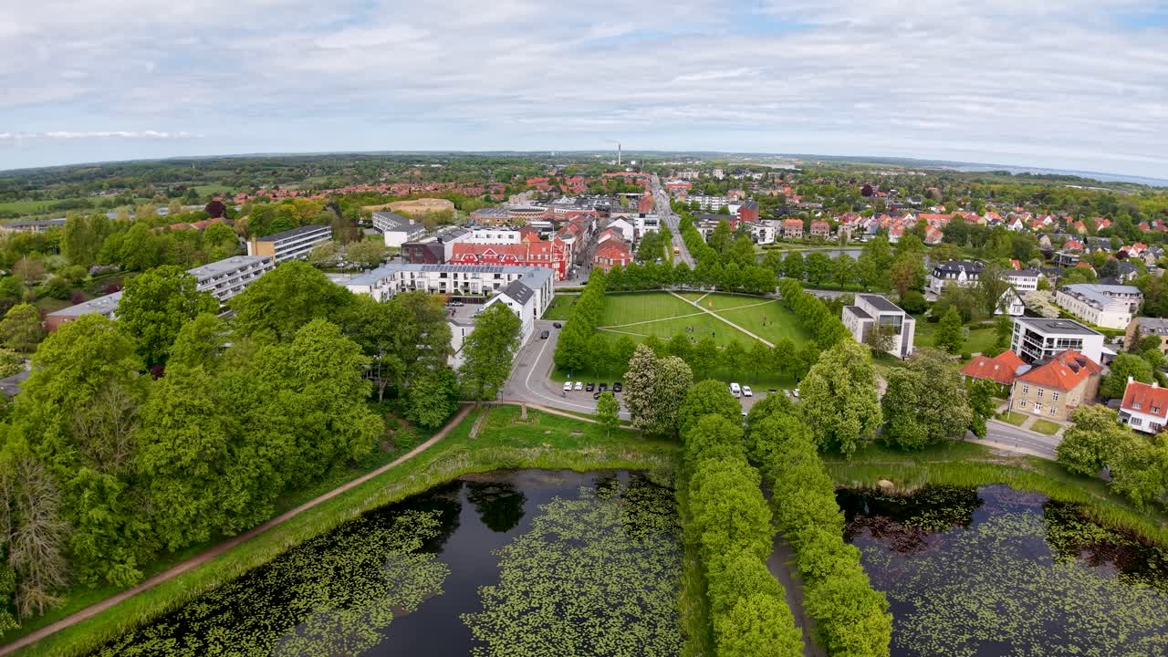Drone footage of a tree-lined canal and park in downtown Aarhus, Denmark, with water, greenery and red-roof buildings