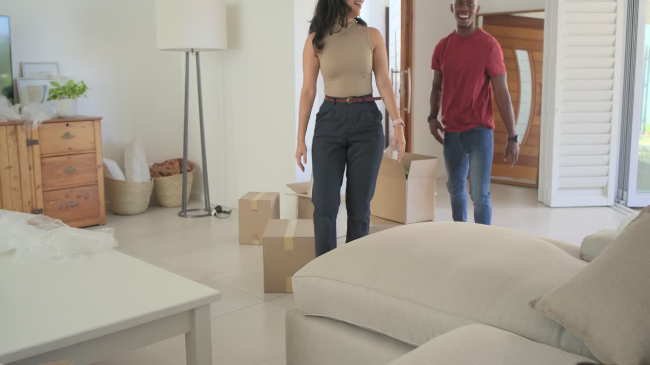 Diverse family with youth son entering home carrying boxes into living room, unpacking, settling in