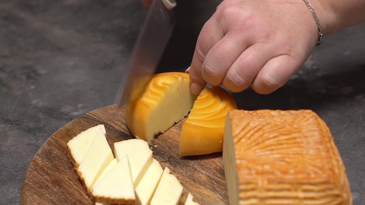 Mano che taglia formaggio artigianale su un tagliere di legno per un piatto degustazione, mano che taglia formaggio giallo a pezzi su un tagliere di legno, preparando uno spuntino delizioso