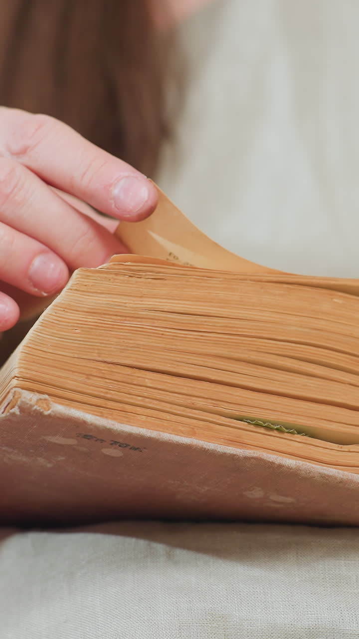 여린 손으로 소중한 가보 책 페이지를 넘기는 모습, 부드러운 니트 스웨터를 입고 따뜻한 뉴트럴 톤으로 인쇄된 일러스트를 따라 그리는 백인 엄마, 바느질로 제본된 책등과 누렇게 변색된 종이, 감상적이고 조용하며 부드러운 분위기