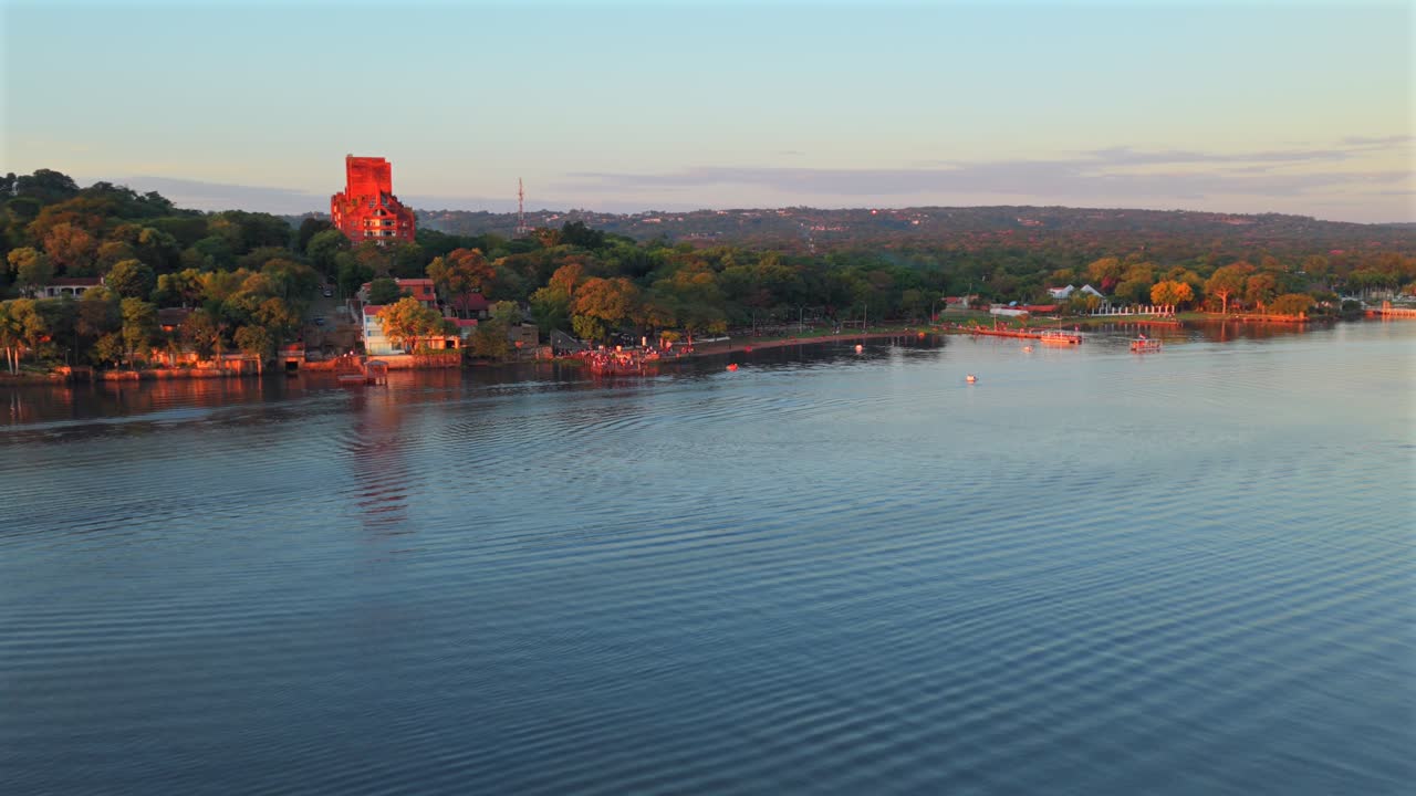Alto hotel abbandonato in mattoni rossi circondato da alberi e dalla costa lungo il lago Ypacaraí, San Bernardino, Paraguay, durante l'ora d'oro