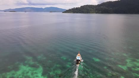 aerial view over traditional longtail boat travelling across tranquil waters in koh lipe