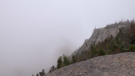 A-Hiker-Walks-up-to-and-Stands-on-the-Edge-of-a-Cliff-in-Ominous-Foggy-Weather-in-the-Adirondack-Mountains-of-New-York,-Wide-Angle