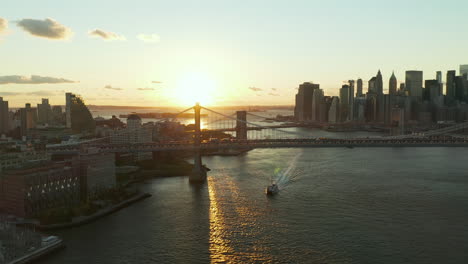 Impresionantes-Vistas-Aéreas-Del-Crucero-Que-Pasa-Por-Debajo-Del-Puente-De-Manhattan-Al-Atardecer.-Rascacielos-Del-Centro-En-El-Paseo-Marítimo-De-Fondo.-Manhattan,-Ciudad-De-Nueva-York,-Estados-Unidos