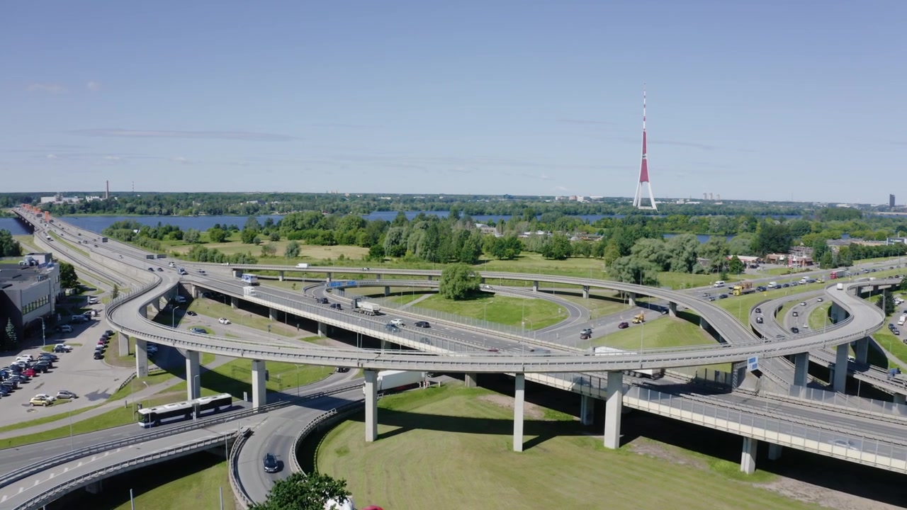 High angle drone view of modern road interchange infrastructure with the iconic Riga TV tower in background. Traffic in city.