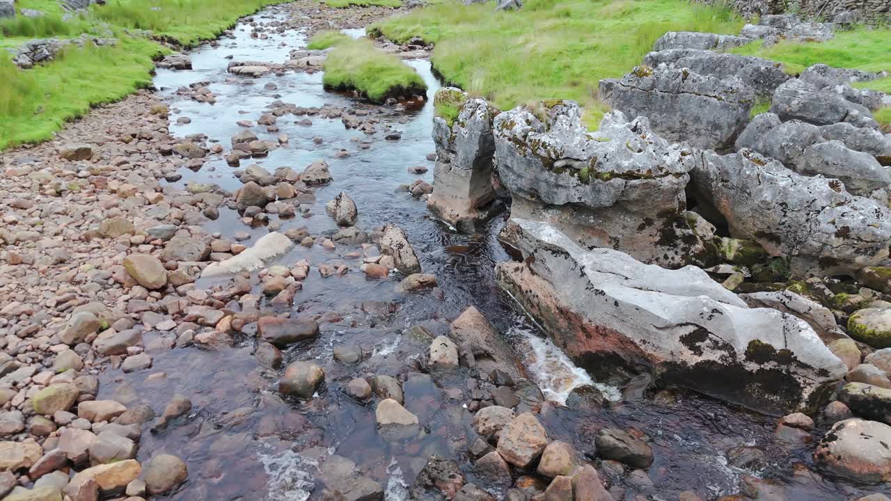 A rocky stream with clear flowing water through a green landscape