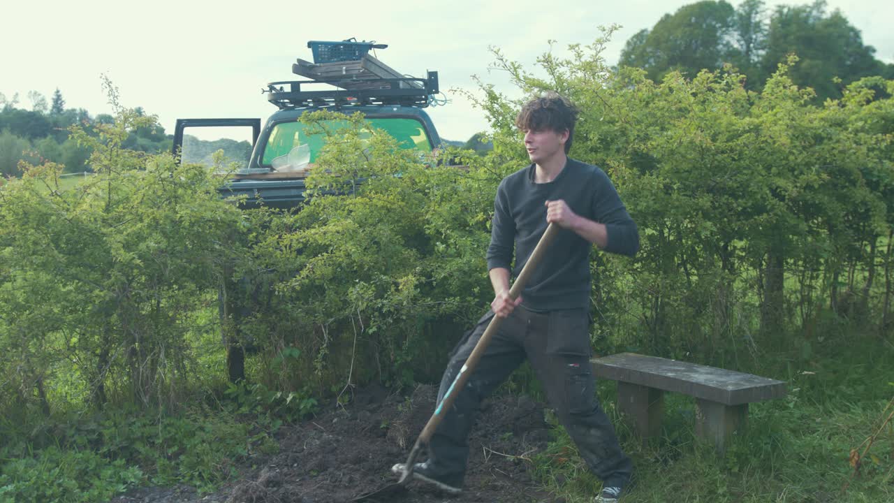 픽업 트럭 침대에 울타리를 통해 토양을 삽질하는 젊은 남자