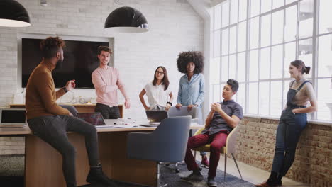 six millennial creative colleagues in discussion in an office meeting room, full length