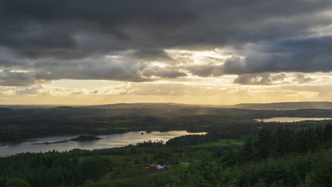 time lapse of rural landscape with visible farmhouse located near local lake, forest and hills during a cloudy evening sunset viewed from above lough meelagh in county roscommon in ireland