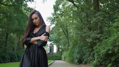 Brunette-wearing-a-black-dress-and-high-heels-walking-in-a-national-park-in-Belgium,-surrounded-by-trees