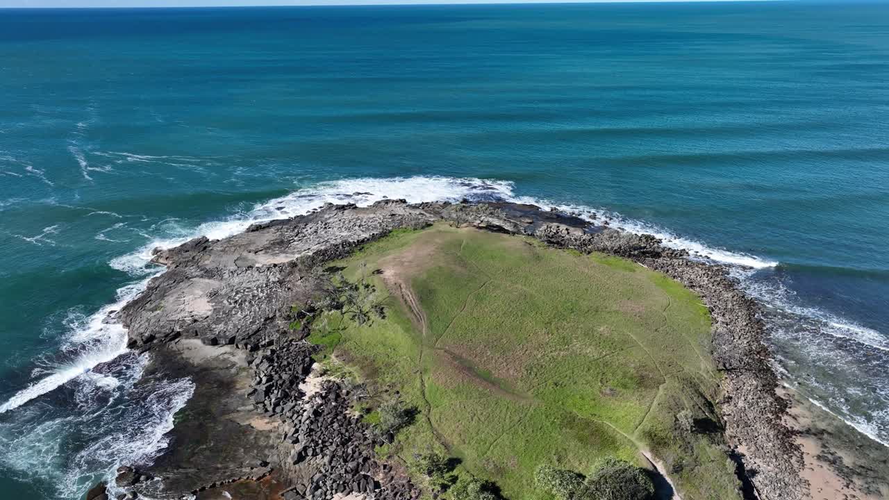 Volando basso su un promontorio roccioso ed erboso, la telecamera avanza mentre onde spumeggianti si infrangono sulle rocce nere sottostanti, con spruzzi bianchi che si levano contro la costa scura e frastagliata. Drone DJI 4K.