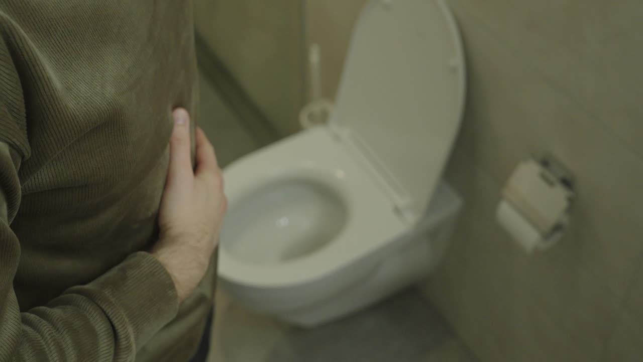 Realistic top-down scene of a man standing next to a toilet, holding his stomach in discomfort, symbolizing digestive problems, bloating, abdominal pain, and everyday gastrointestinal issues at home