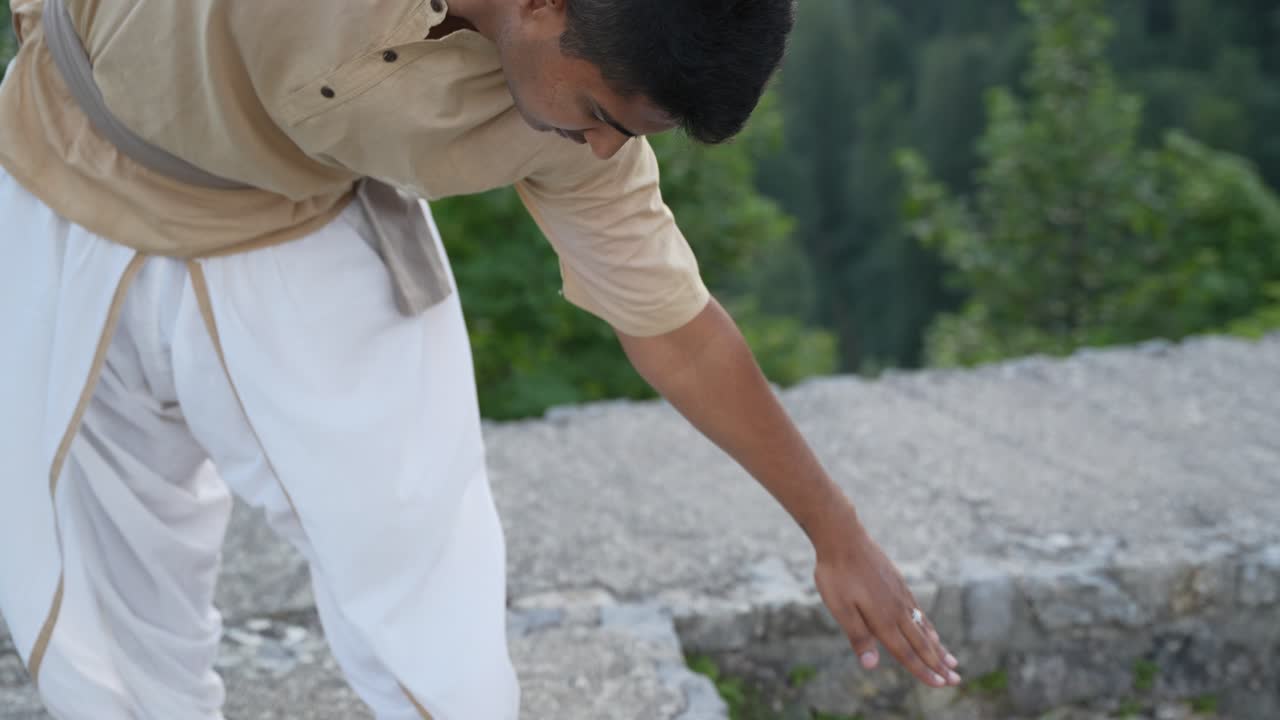인도 성인 남성이 눈을 감고 요가를 하고 손으로 땅을 만지고 돌 성벽에 맨발로 서서 포즈를 준비하고 있습니다.