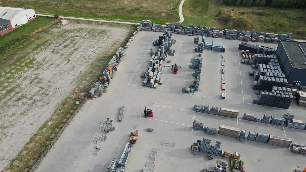 Aerial overview of forklift trucks driving over a neatly organized industrial storage yard on a sunny day