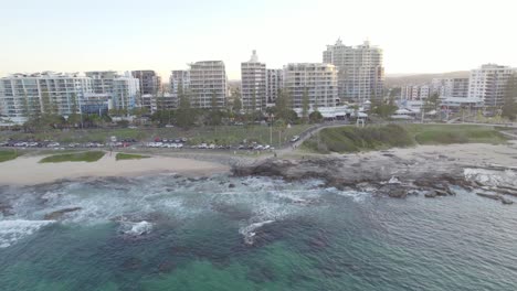 Wellen-Plätschern-An-Der-Felsigen-Küste-Mit-Panorama-Der-Unterkunftsgebäude-Entlang-Der-Mooloolaba-Promenade-An-Der-Sunshine-Coast-In-Queensland,-Australien