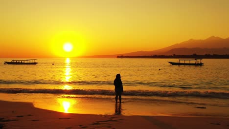 bali, indonesia, atractiva dama asiática relajándose en la arena blanca de la playa tropical admirando la dorada puesta de sol