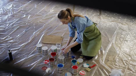 mujer en el estudio abre diferentes colores de pintura en frascos de metal en el suelo en cámara lenta