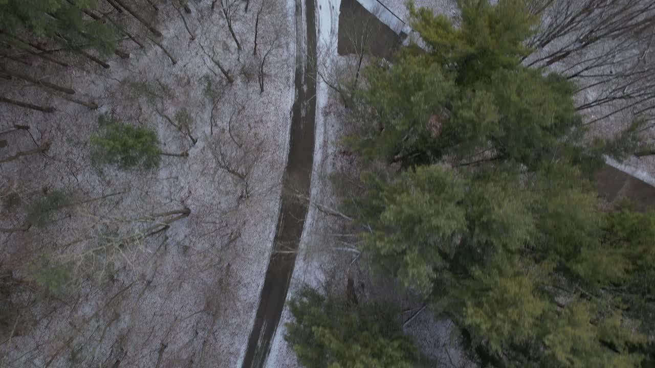 una vista de arriba hacia abajo directamente sobre un camino de tierra con nieve y pinos, algunos árboles están desnudos