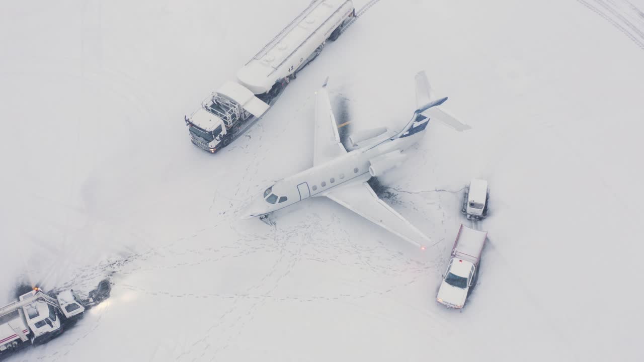 бизнес-джет "эмбраер" на заснеженном асфальте с машинами поддержки, аэрофотосъемка