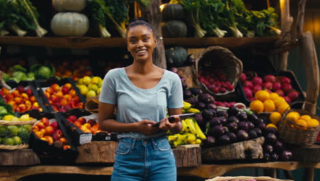 portrait of smiling woman with digital tablet working at fresh fruit and vegetable stall in market