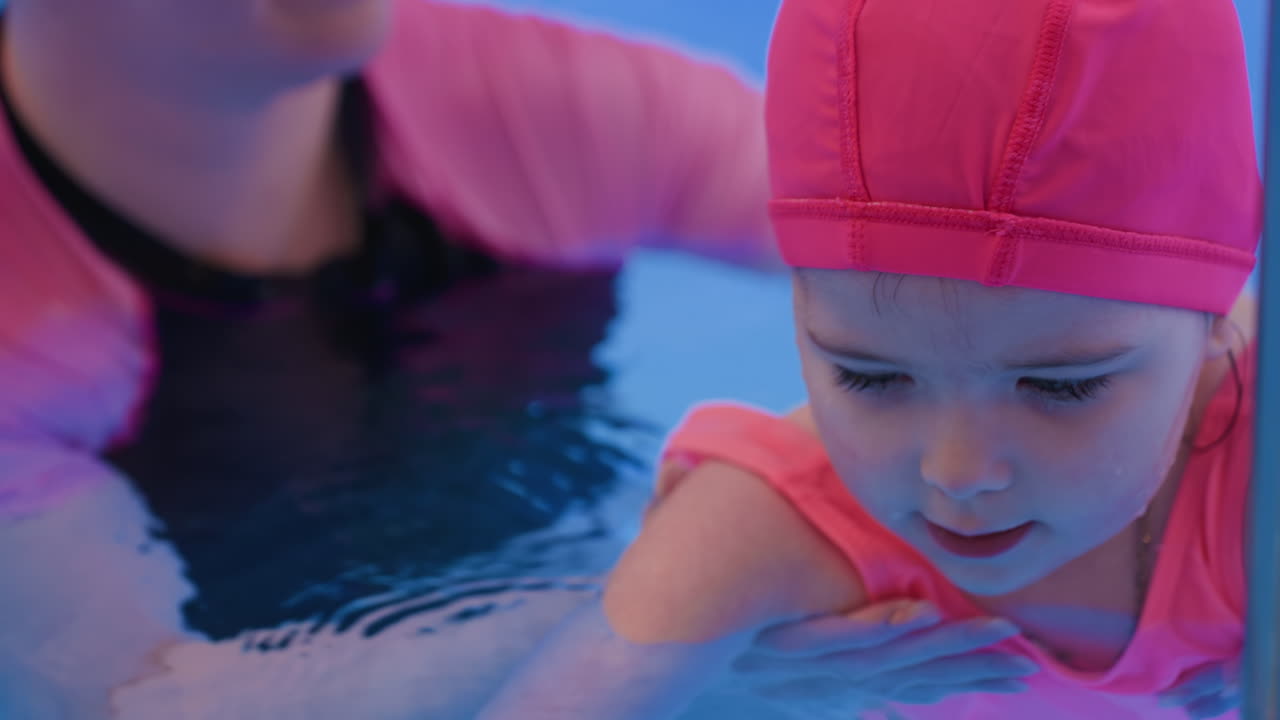 Head capturing of small child resting peacefully in pool water, face partly immersed with calm expression, highlighting innocence, aquatic freshness, and tenderness under soft lighting reflection