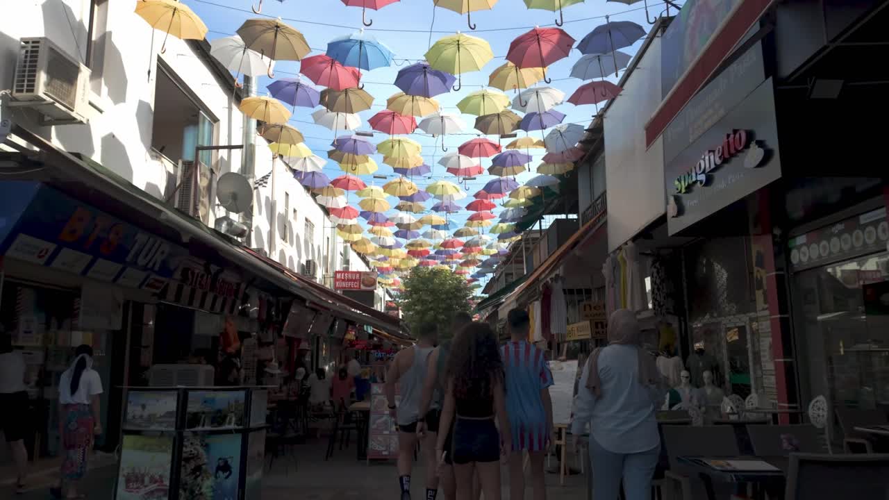 A lively street in Antalya adorned with colorful umbrellas providing shade and a cheerful atmosphere for visitors.