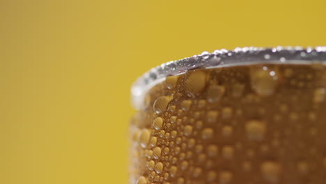 acercamiento de gotas de condensación en una lata giratoria de cerveza fría o refresco para llevar contra un fondo amarillo con espacio de copia 1