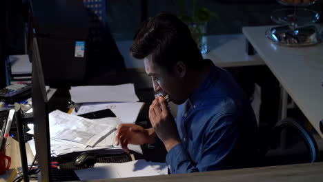 young office worker is working late into the night at his desk in office, he grapples with stress and anxiety as deadlines loom and exhaustion sets in