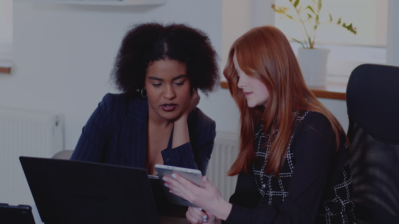 Two Business Women Discussing Work on Tablet and Laptop