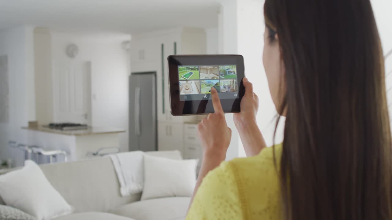 vista posterior de una mujer asiática usando una tableta con la vista de las cámaras de seguridad en casa