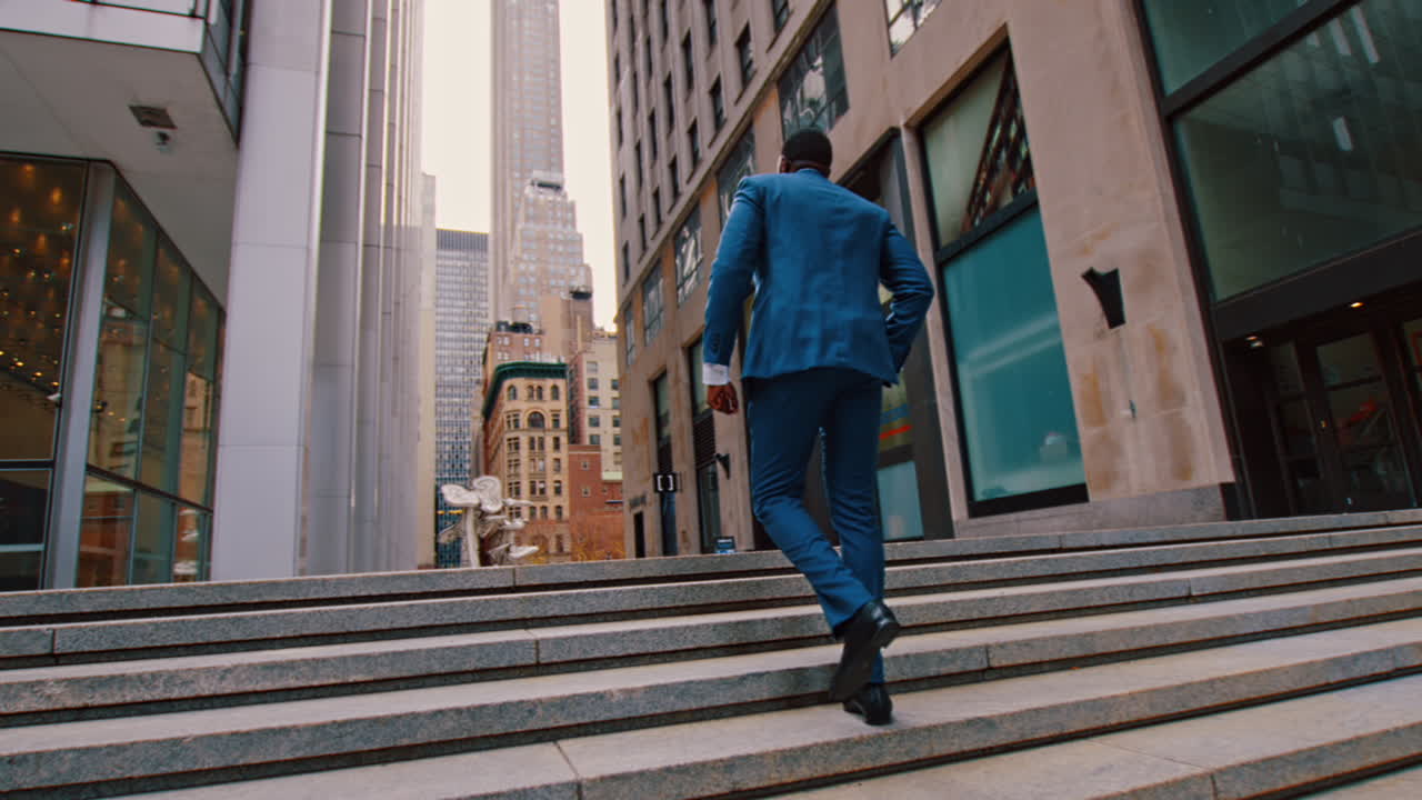 New York, USA, 28 May 2025: Businessman in blue suit walking up stairs in New York. Rear view of American man walking up stone stairs towards office buildings in New York City