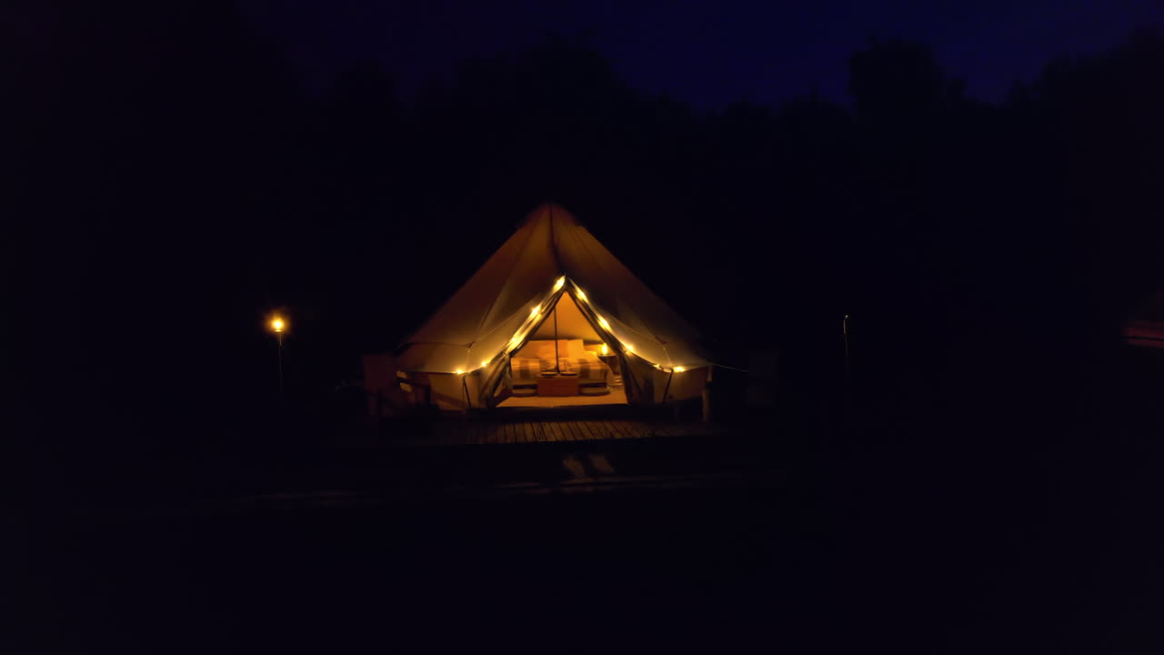 Tende con torce accese, lampade e sedie di legno al glamping, foresta circostante, notte