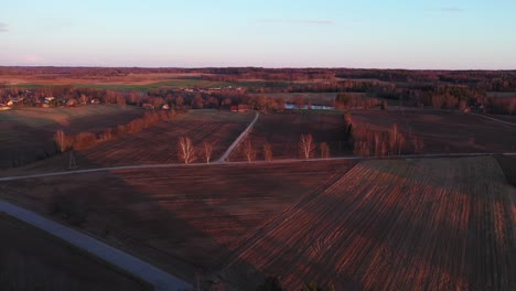 plowed crop fields in rural village at sunset, aerial tracking drone