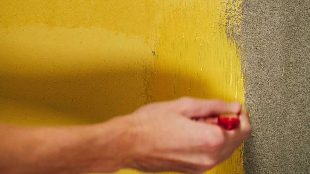 Primo piano di una mano che dipinge una parete con vernice gialla