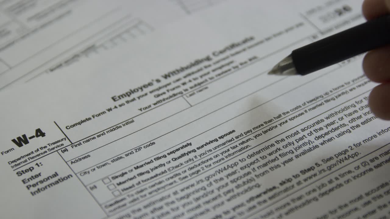 Close up of person filling out a W-4 form. Employment withholding certificate. Person filling out tax form from IRS