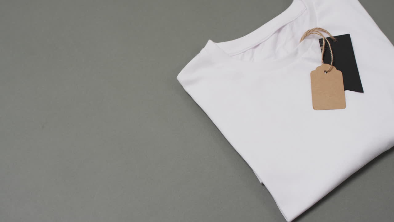 Video of flat lay of white t shirt with tags and copy space on grey background