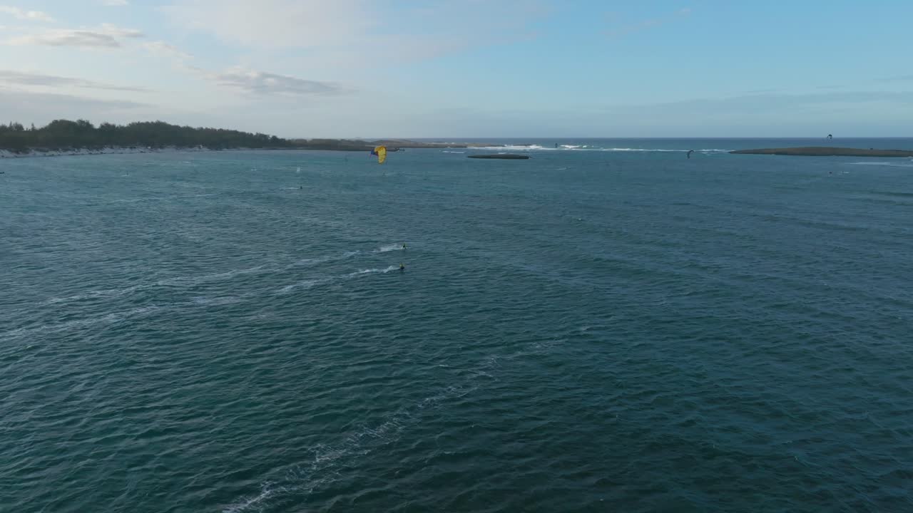 Drone captures kitesurfers riding in various directions over choppy sea with visible coastline and vegetation