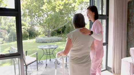 assisting elderly asian woman with walker, caregiver providing support at home