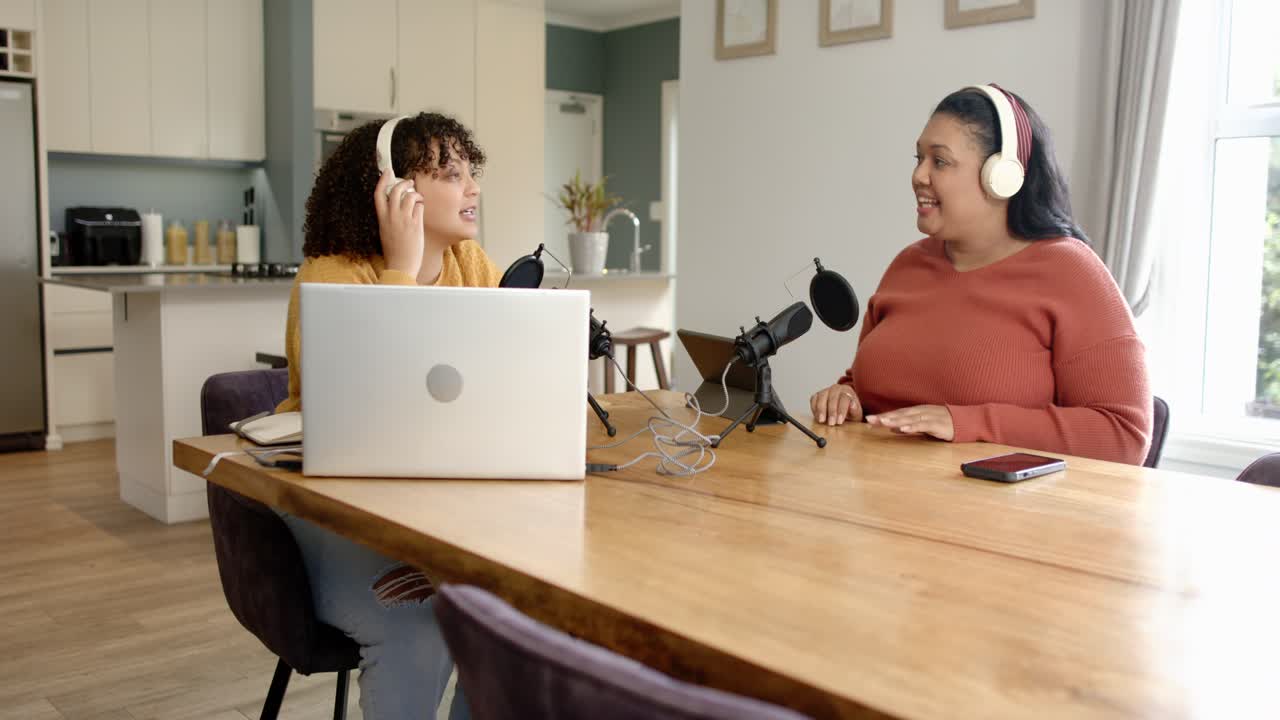 Ascoltando il playback, due co-conduttrici in cucina con microfoni controllano l'audio, ridendo.