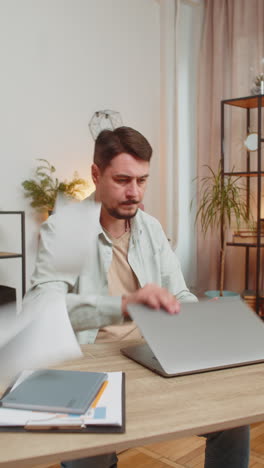stressed upset young man freelancer looking at unpaid bank debt bills sitting at home office desk