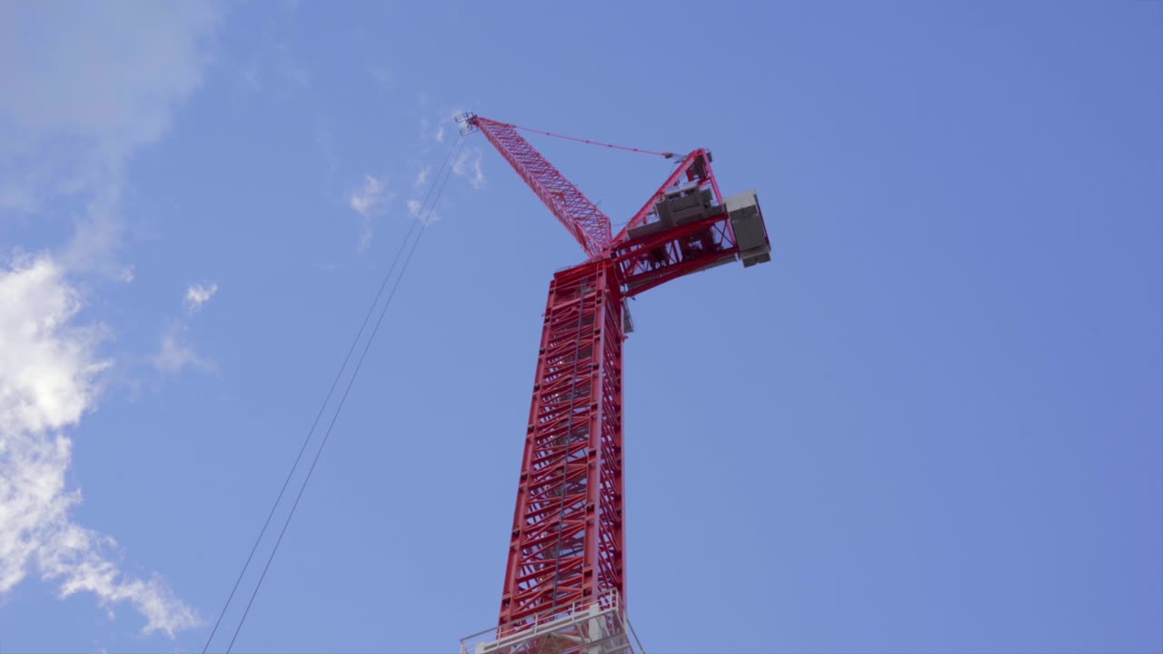 푸른 하늘을 가로질러 지나가는 구름을 올려다보는 빨간 건설 기중기 팔 아래