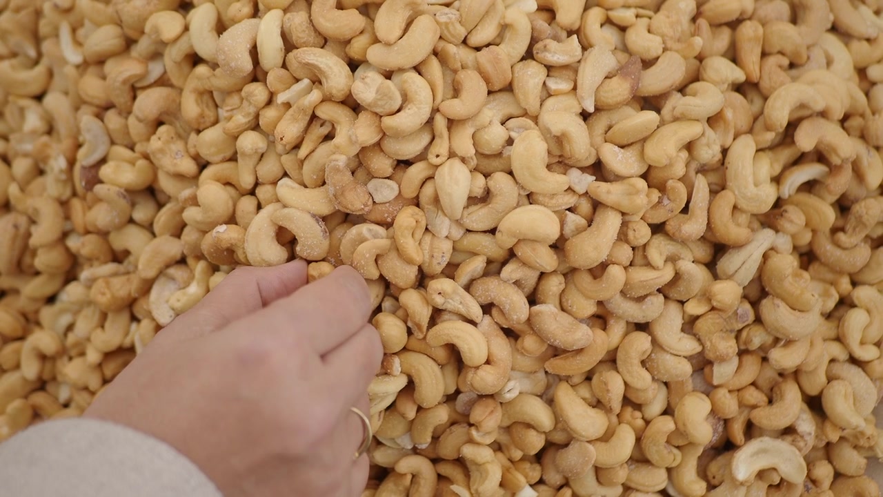 Hånd som plukker ristede cashewnøtter fra en stor haug