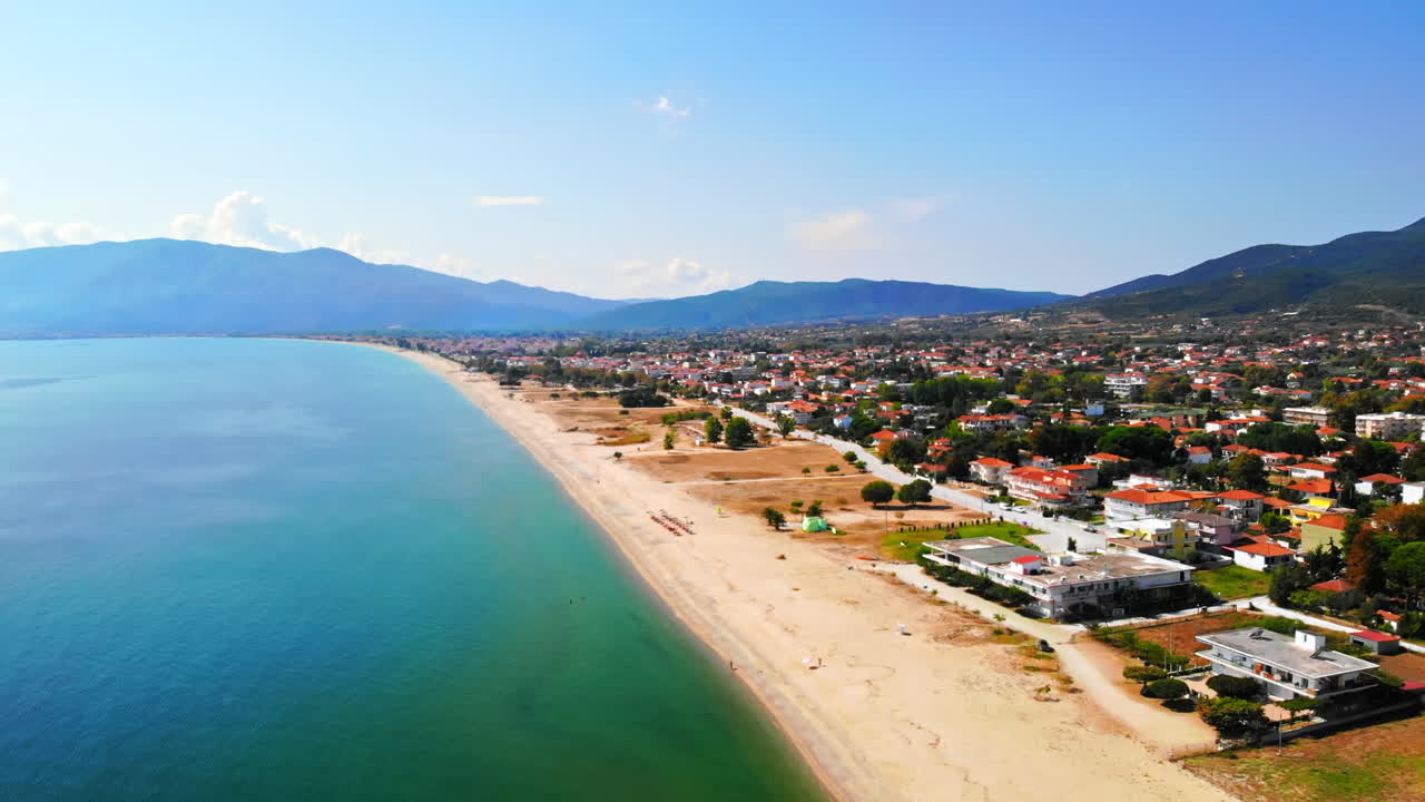 Panorama of the Asprovalta with multiple buildings and greenery, green hills on the background. Aegean sea coast. Long beach along the town. Sunny day. Greece