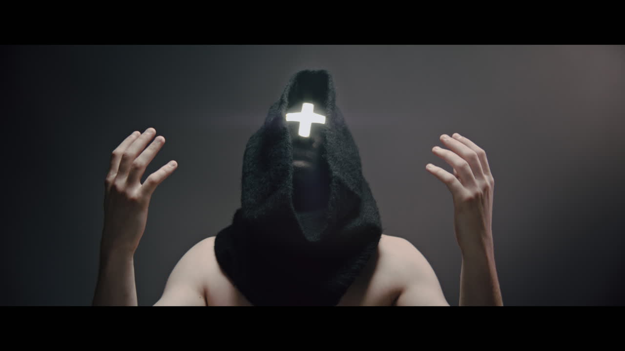 Masked man with cross of light glowing on his face prays