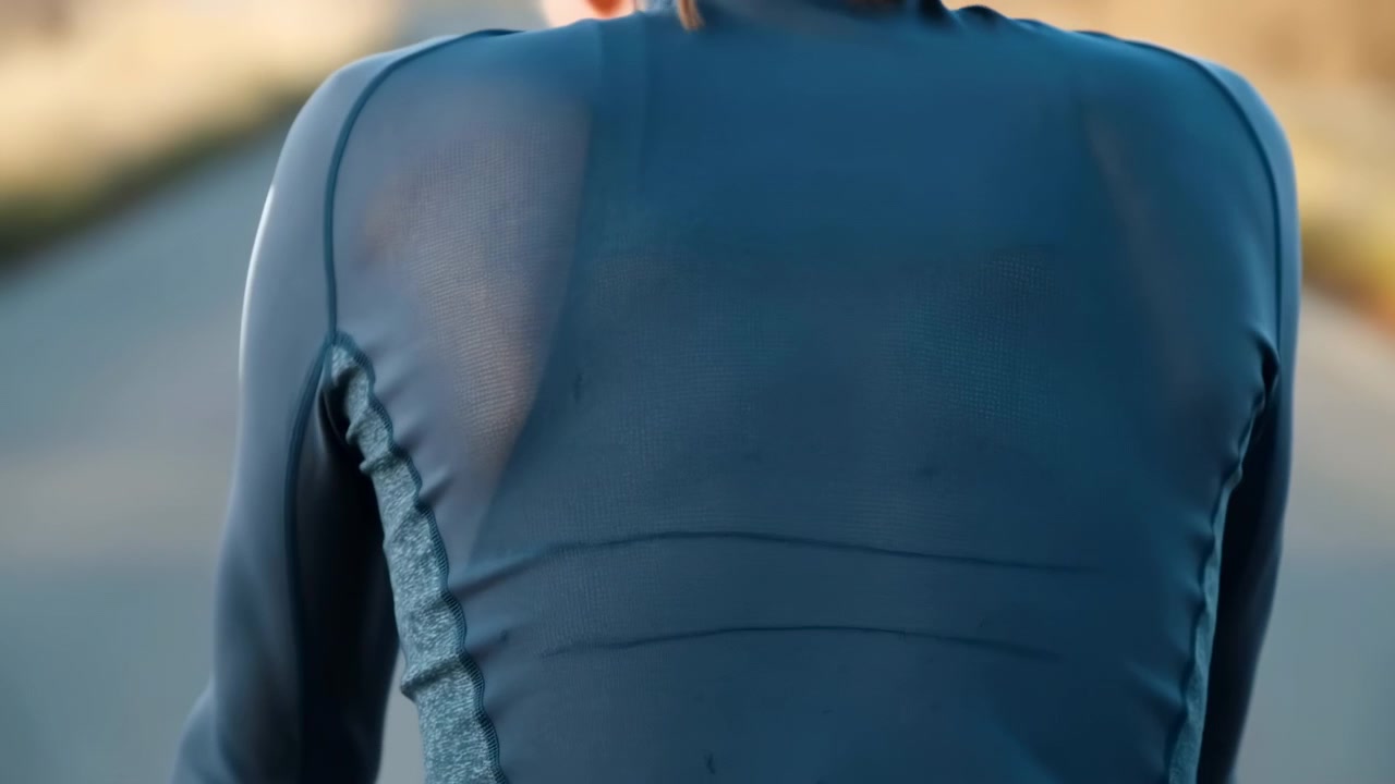 Close torso framing follows a person wearing a dark blue long-sleeve garment outdoors, with gentle body movement, warm side light, visible seams, and softly blurred surroundings.
