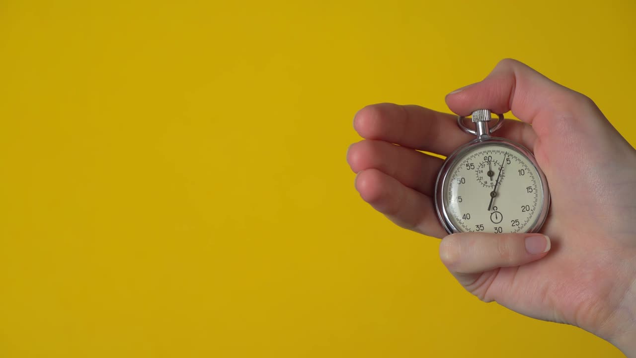 La mano di una donna tiene un cronometro analogico su sfondo giallo